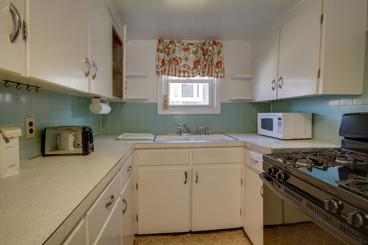 Cozinha com armários brancos, fogão, micro-ondas e janela com valance floral.