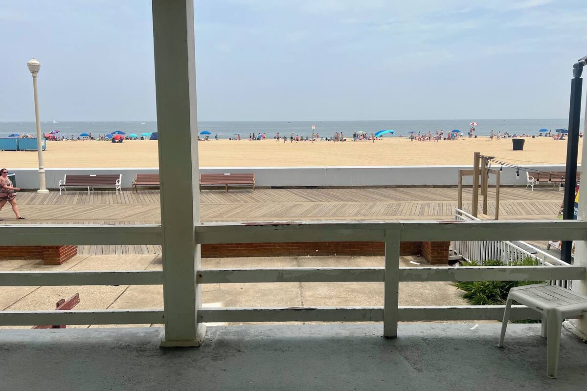Vista a la playa desde una terraza cubierta con bancos de madera y barandilla.