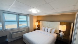 A hotel room with a large bed, two bedside tables with lamps, a window with blinds, and a ceiling light. - Majestic Hotel & Apartments (Ocean City)