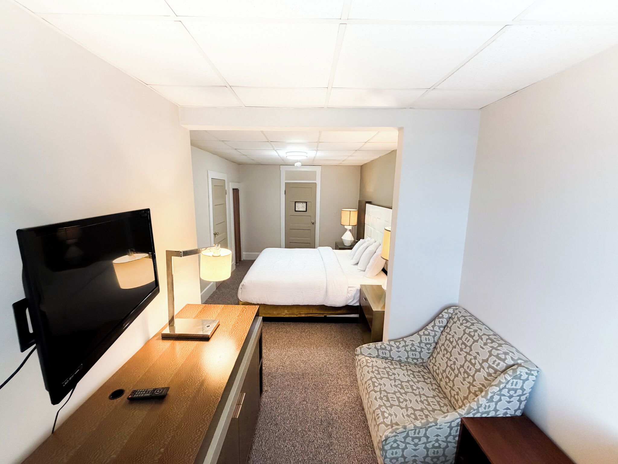 Hotellihuone, jossa on sänky, televisio, työpöytä, tuoli ja sohva.