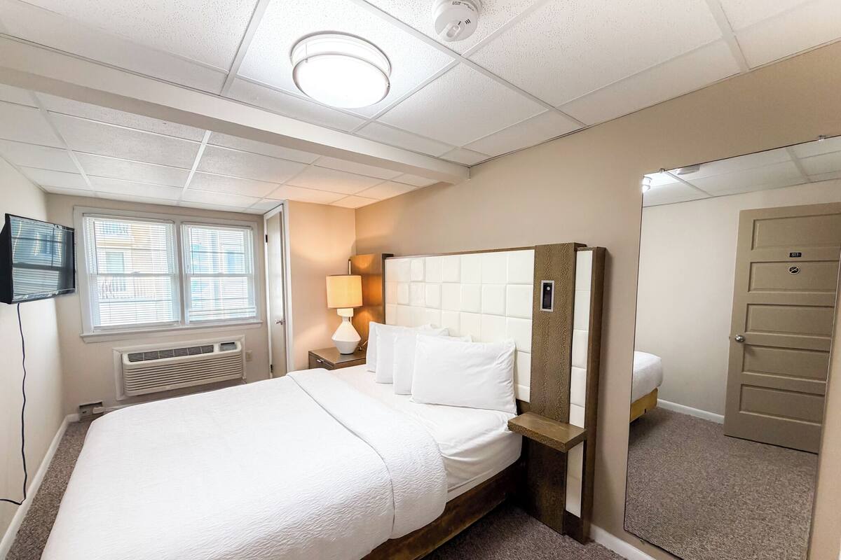 Habitación de hotel con cama, lámpara de noche, televisión y espejo.