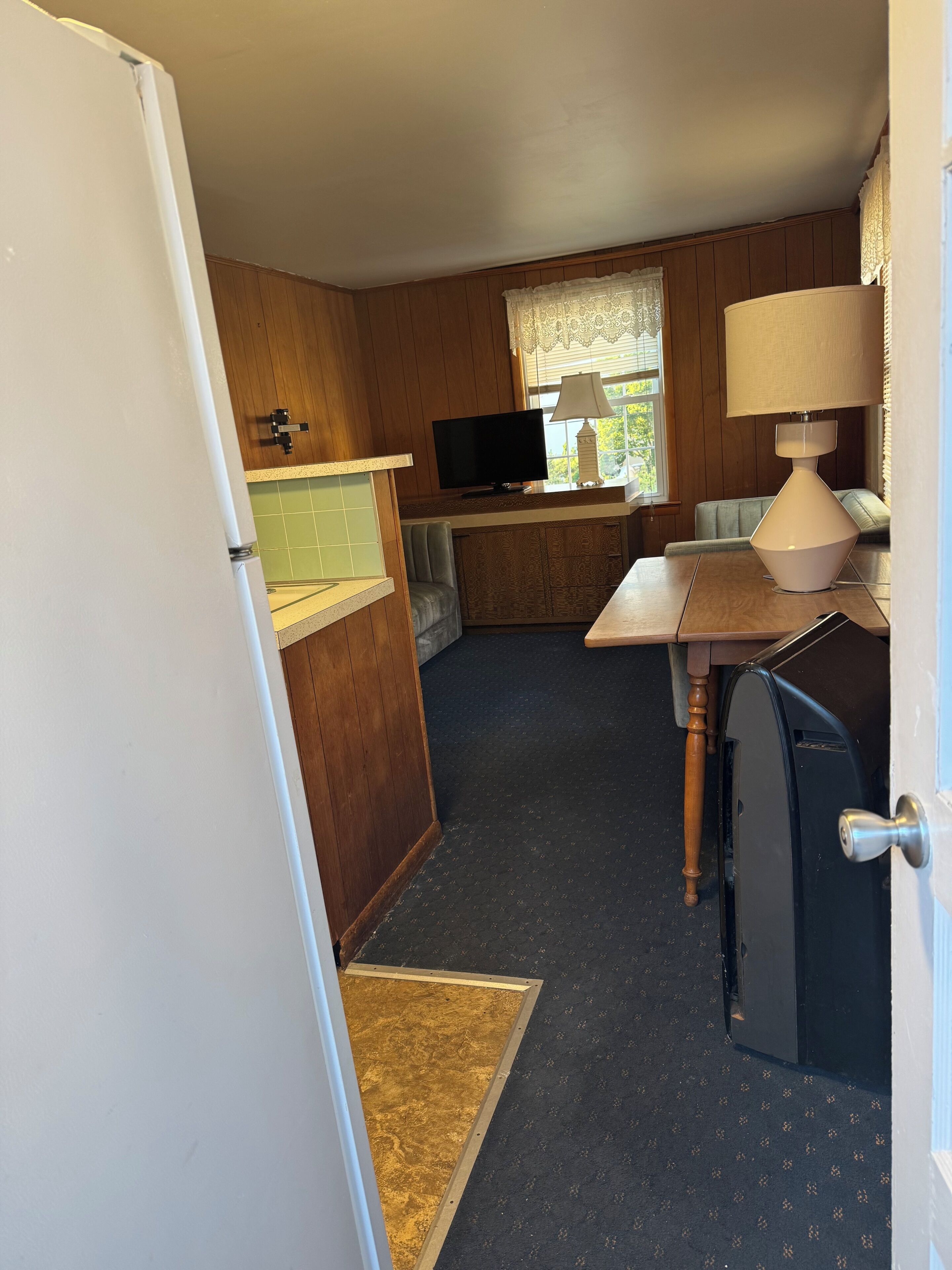 A compact kitchen with wooden cabinets, a television, and a lamp.