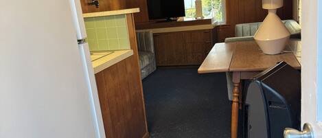 A compact kitchen with wooden cabinets, a television, and a lamp.