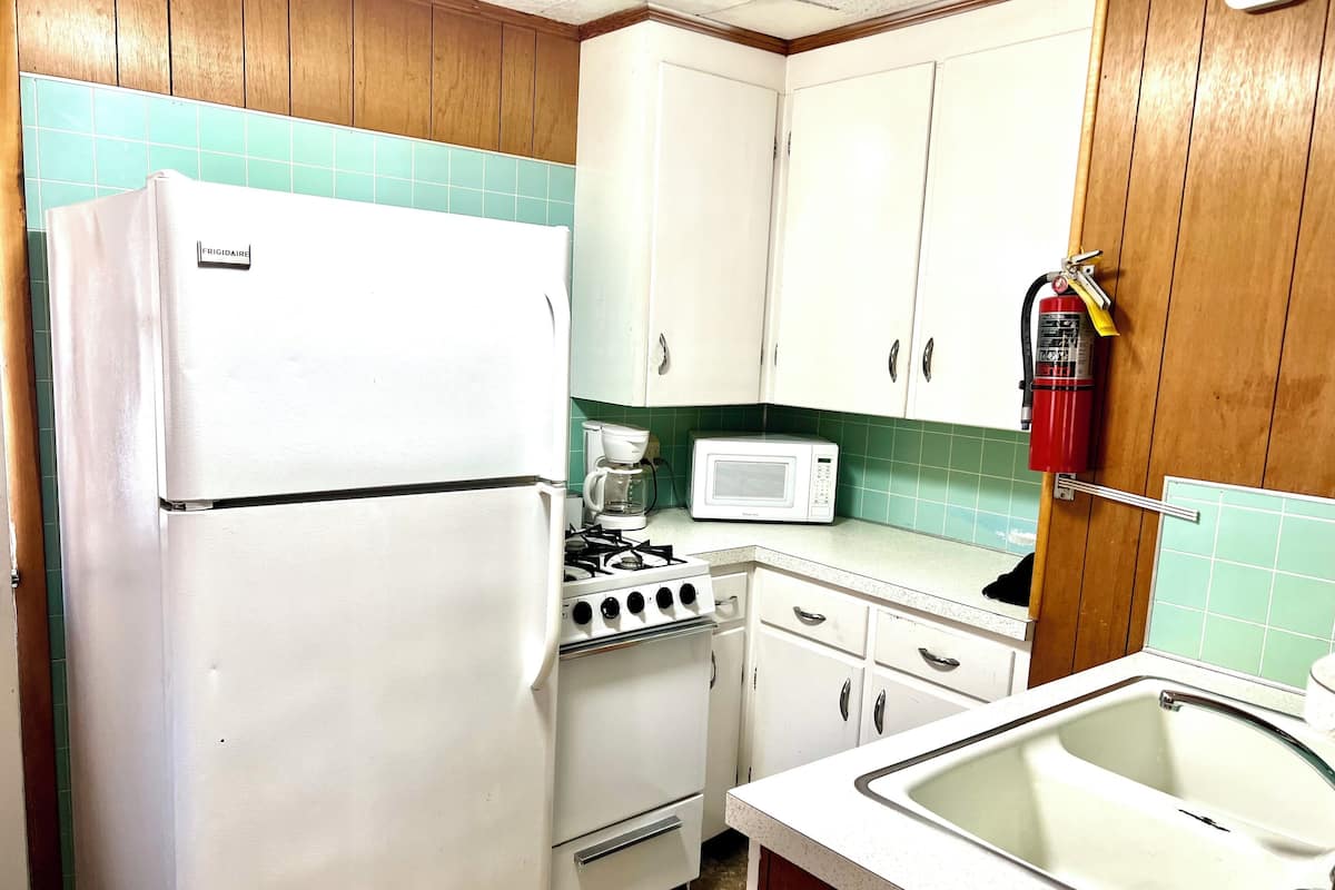 Una cocina compacta con electrodomésticos blancos, estufa a gas, microondas y un lavamanos.