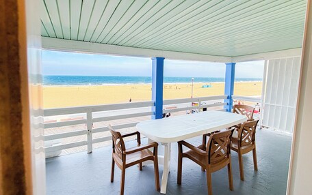 A covered patio with a table and chairs, overlooking a beach.
