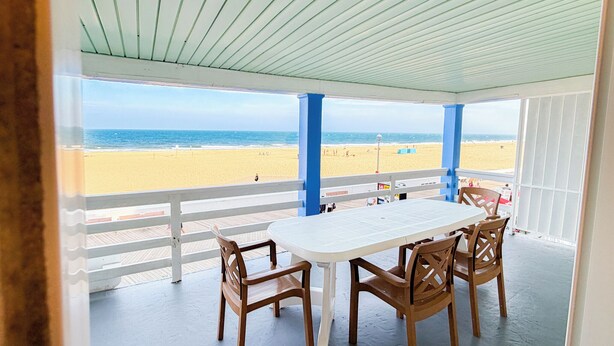 A covered patio with a table and chairs, overlooking a beach. - Majestic Hotel & Apartments (Ocean City)