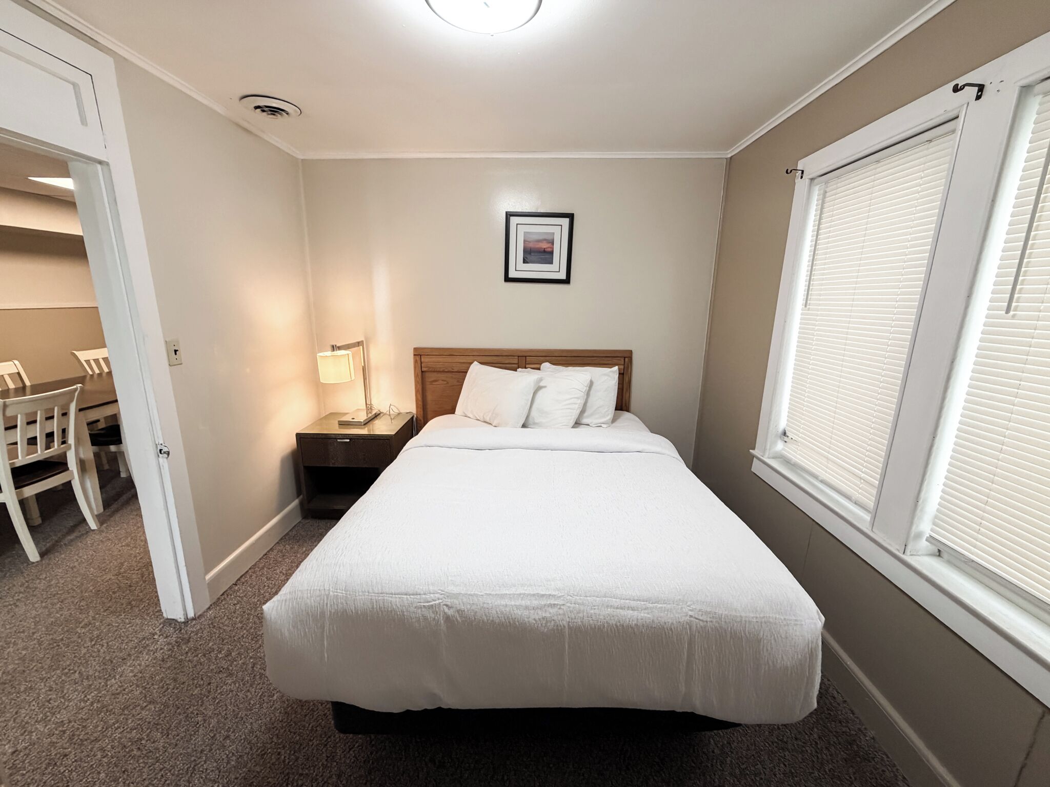 A bedroom with a bed, bedside table, lamp, and a window with blinds.