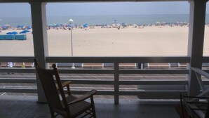A beach view from a covered area with a wooden chair and a railing. - Majestic Hotel & Apartments (Ocean City)