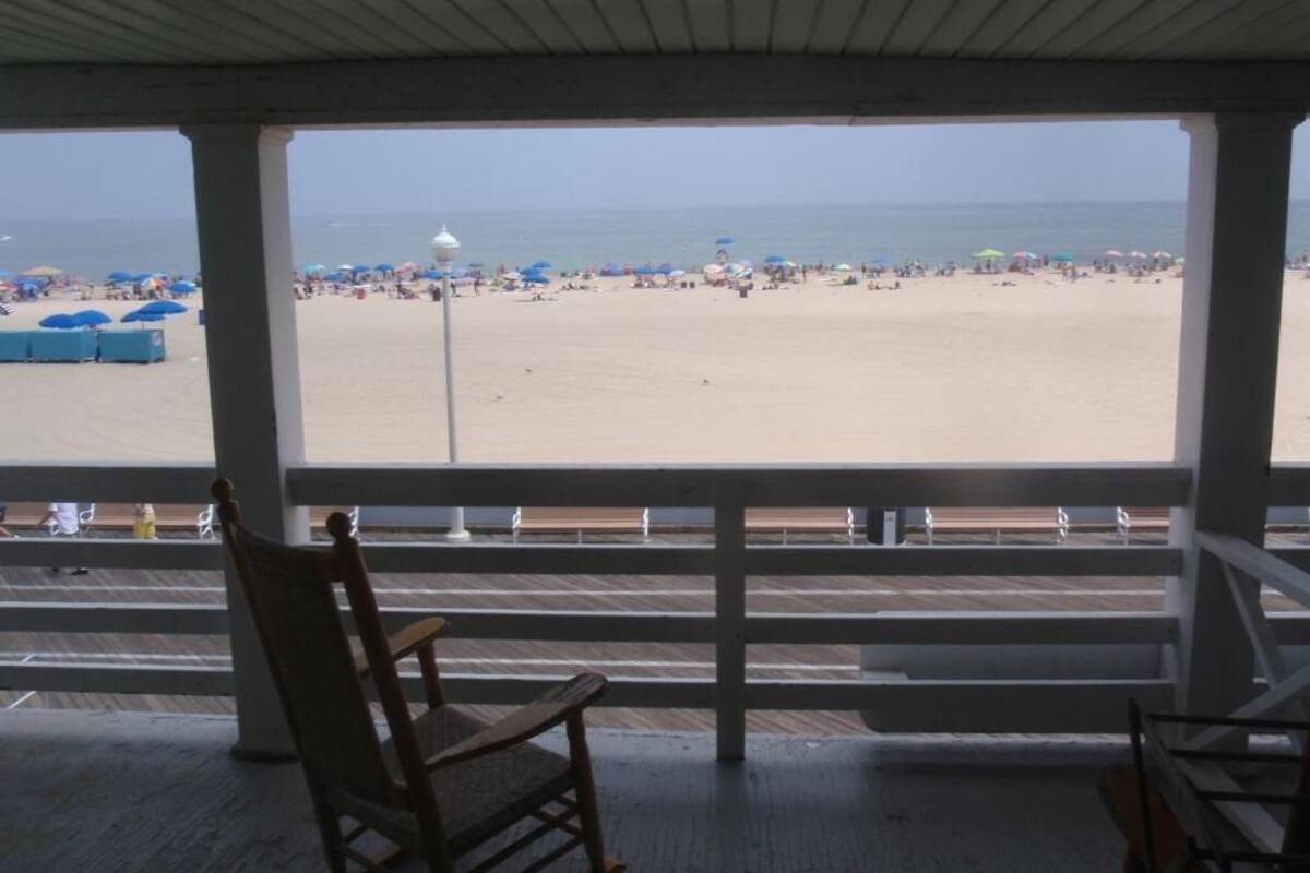 Vista a la playa desde un espacio cubierto con una silla de madera y una barandilla.