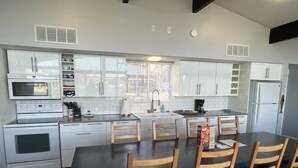 Una cocina moderna con armarios blancos, una isla central, una mesa de comedor con sillas y electrodomésticos integrados.