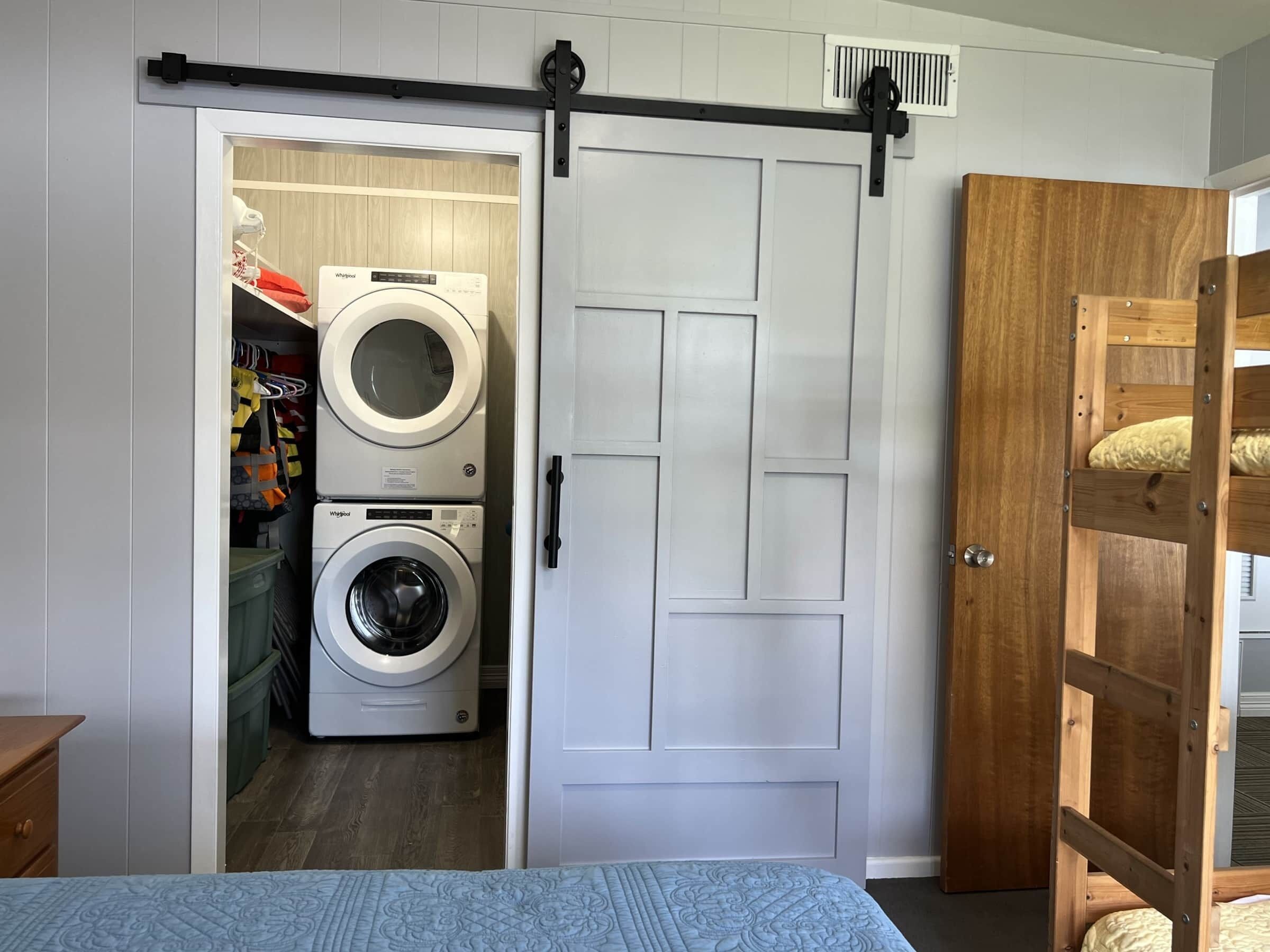 Une chambre comprenant un lit, un lit superposé en bois, une armoire blanche à porte coulissante et un lave-linge dans la pièce adjacente.