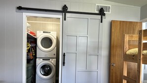 Un dormitorio con una cama, una cama litera de madera, un armario blanco con puerta corredera y una lavadora en la habitación contigua.
