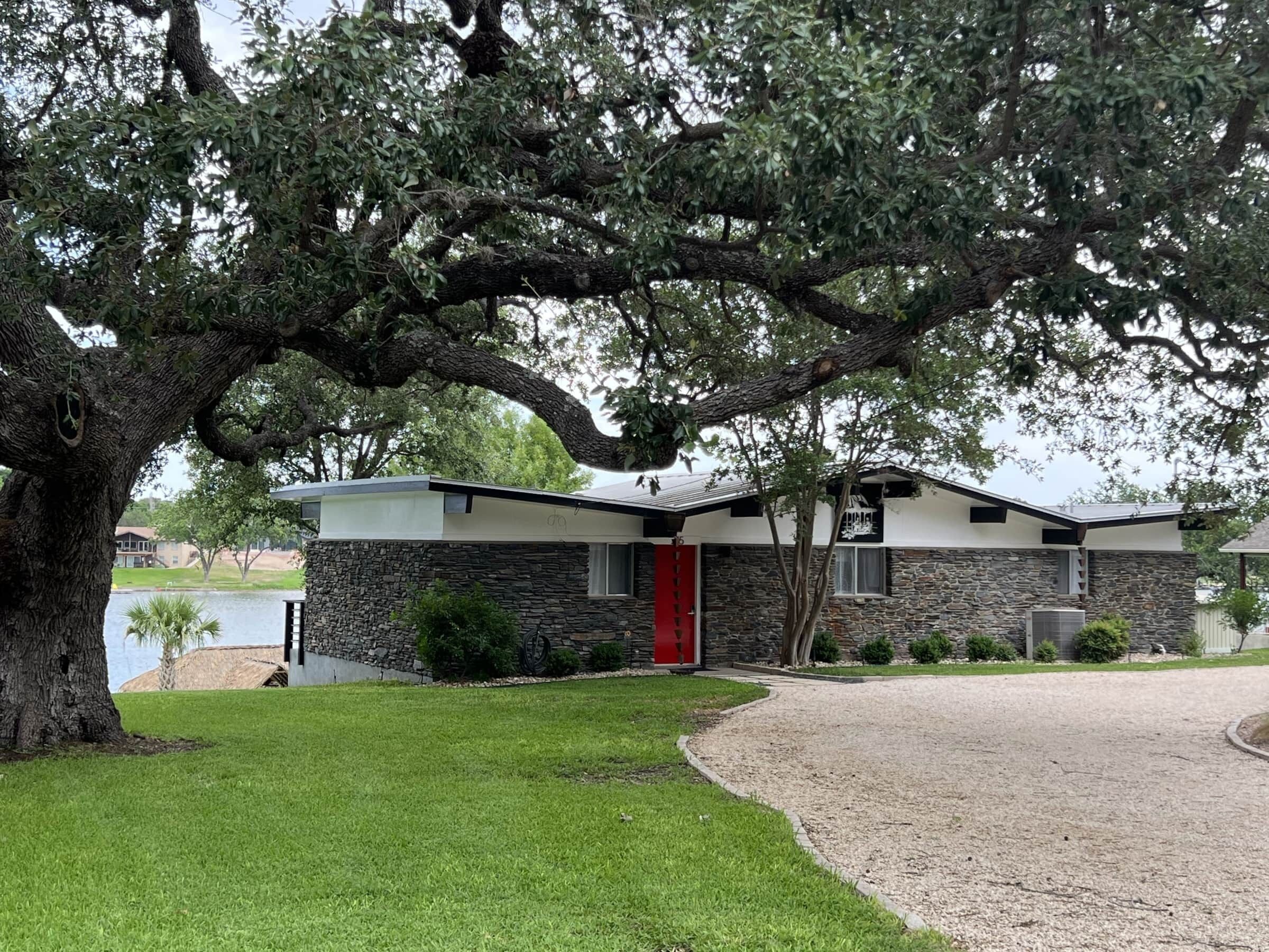 Une maison moderne à deux étages, dotée d’une façade en pierre, d’une porte rouge et d’un grand arbre à l’avant.