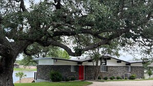 Una casa moderna de dos pisos con fachada de piedra, una puerta roja y un gran árbol en el frente.
