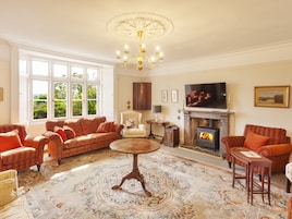 A spacious living room with a fireplace, comfortable seating, and a large window offering a view of greenery.
