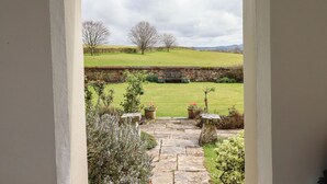 A stone pathway leading to a bench in a garden with a stone wall, flowering plants, and a grassy field with trees in the background. - Crablake Farmhouse (Exeter)