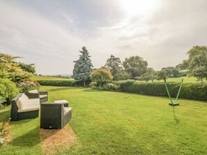 A well-maintained lawn with outdoor furniture, a swing set, and a variety of trees and shrubs.
