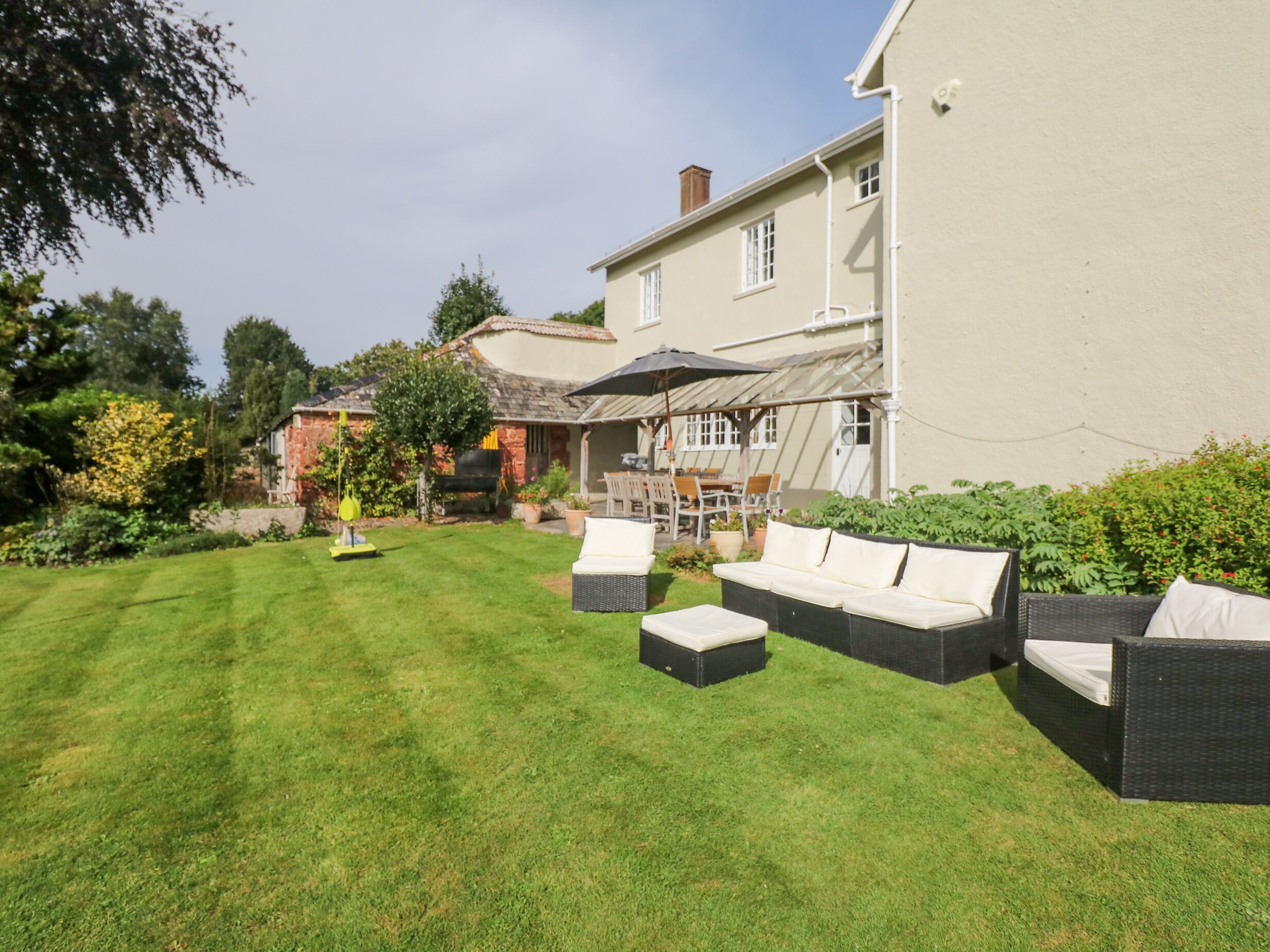 Une pelouse bien entretenue, agrémentée de mobilier d’extérieur, d’un espace barbecue et d’une terrasse avec une table et des chaises.