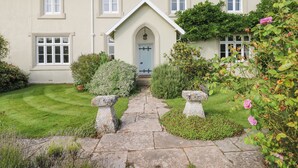 A two-story house with a central entrance, a stone pathway leading to the door, and a well-maintained garden with various shrubs and flowers. - Crablake Farmhouse (Exeter)
