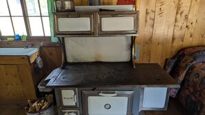 Une cuisinière ancienne dotée de quatre brûleurs, d’un évier et d’un meuble en bois surmonté d’une fenêtre.