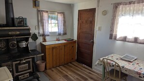 A rustic kitchen with a wood stove, a sink, and a table with a chair.