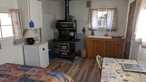A compact room with a bed, a small desk, a stove, a sink, and a window.