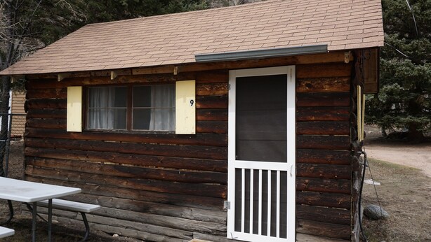 A rustic log cabin with a door, a window, and a picnic table.