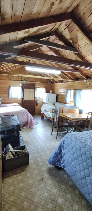 Ein gemütliches Blockhaus mit hohen Decken, Holzwänden, einem Bett, einem Tisch und einem Stuhl.