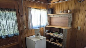 Une cuisine de taille réduite avec des murs en bois, un réfrigérateur, une machine à café et une étagère contenant de la vaisselle et des tasses.