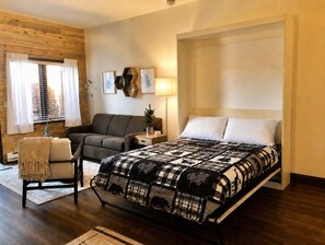 A bedroom with a bed, a sofa, a chair, a lamp, and a window with curtains.