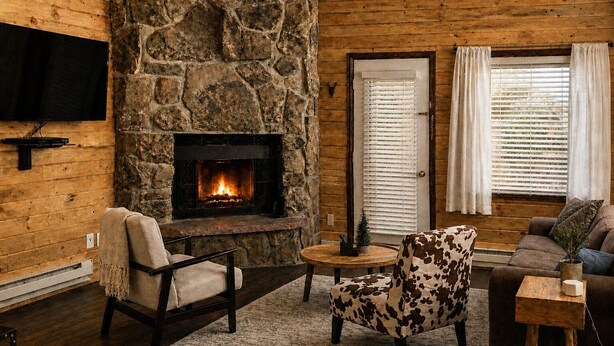 A cozy living room with a stone fireplace, wooden walls, a flat-screen TV, and comfortable seating. - Walkout Studio Near W RMNP + Pool & Hot Tubs (Granby)