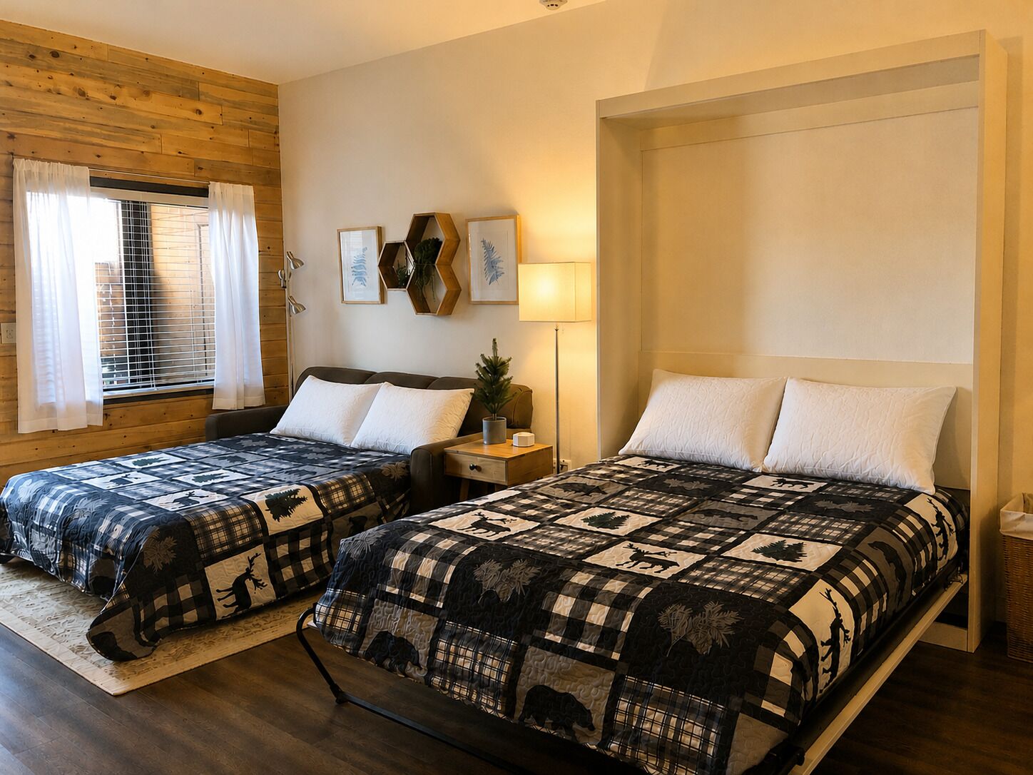 Two beds with matching quilts, a window with curtains, a wall-mounted lamp, and a small plant on a nightstand.
