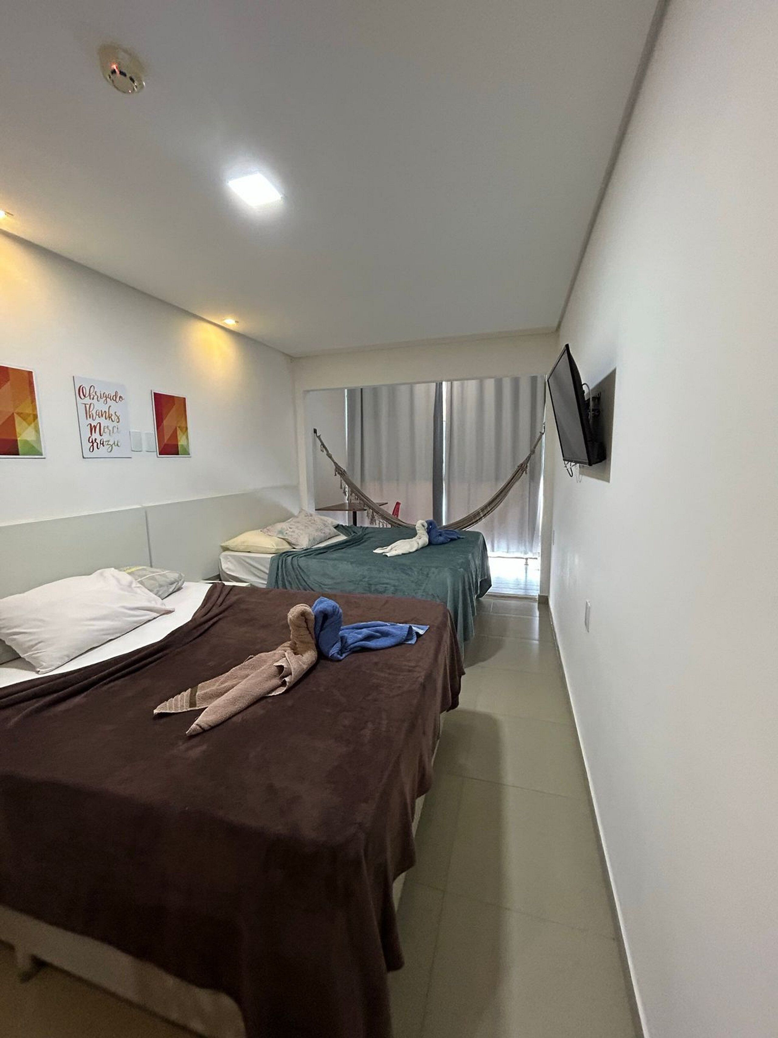Habitación de hotel con dos camas, un televisor montado en la pared y una hamaca.