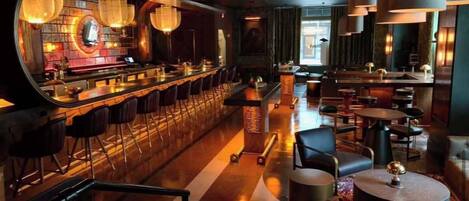 A bar area with a long counter, multiple stools, and hanging light fixtures.