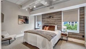 Un dormitorio moderno con una cama grande, un cabecero con panel de madera, una mesita de noche con lámpara y una ventana con vistas.