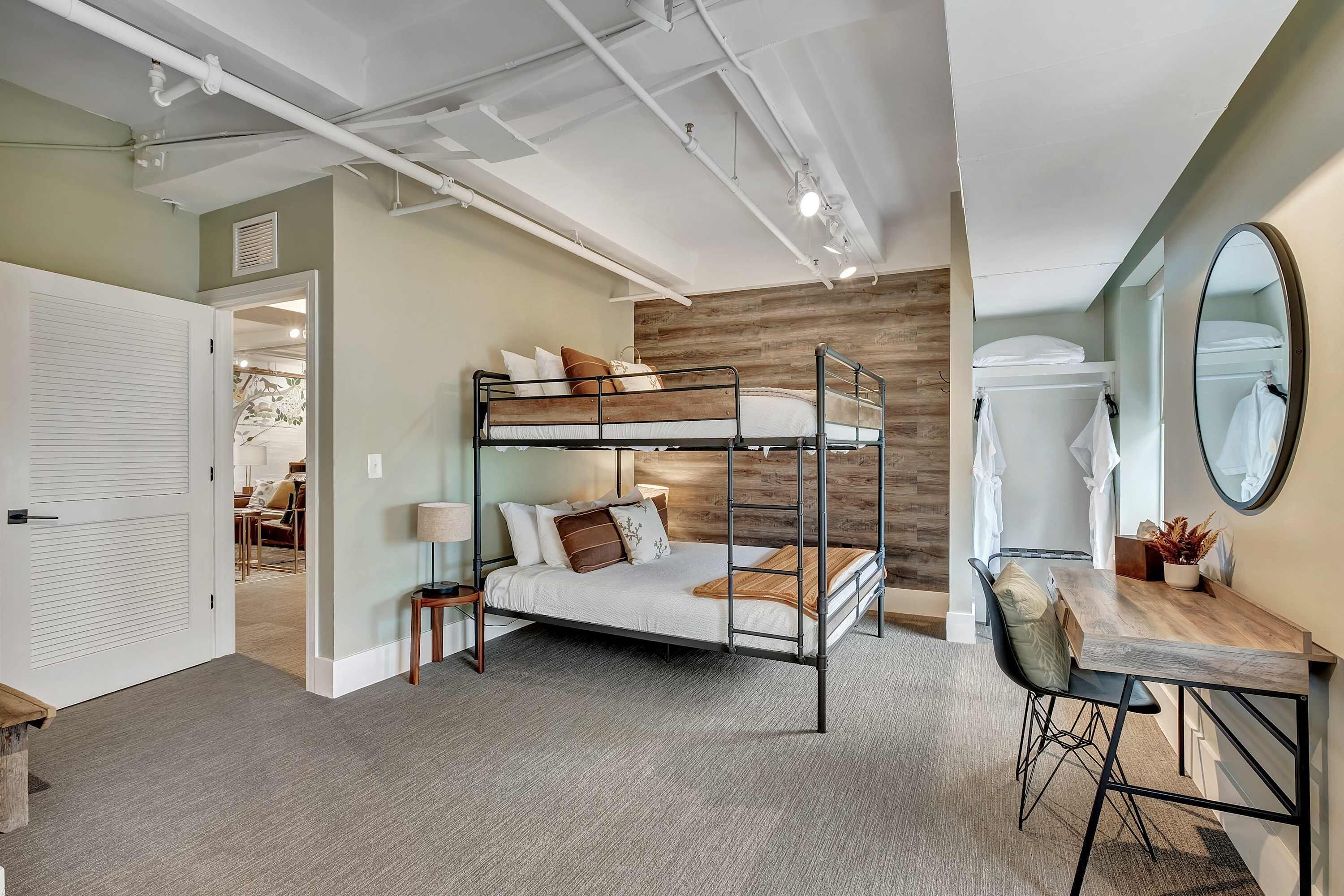 A bunk bed with a desk and chair, a mirror, and a door leading to another room.