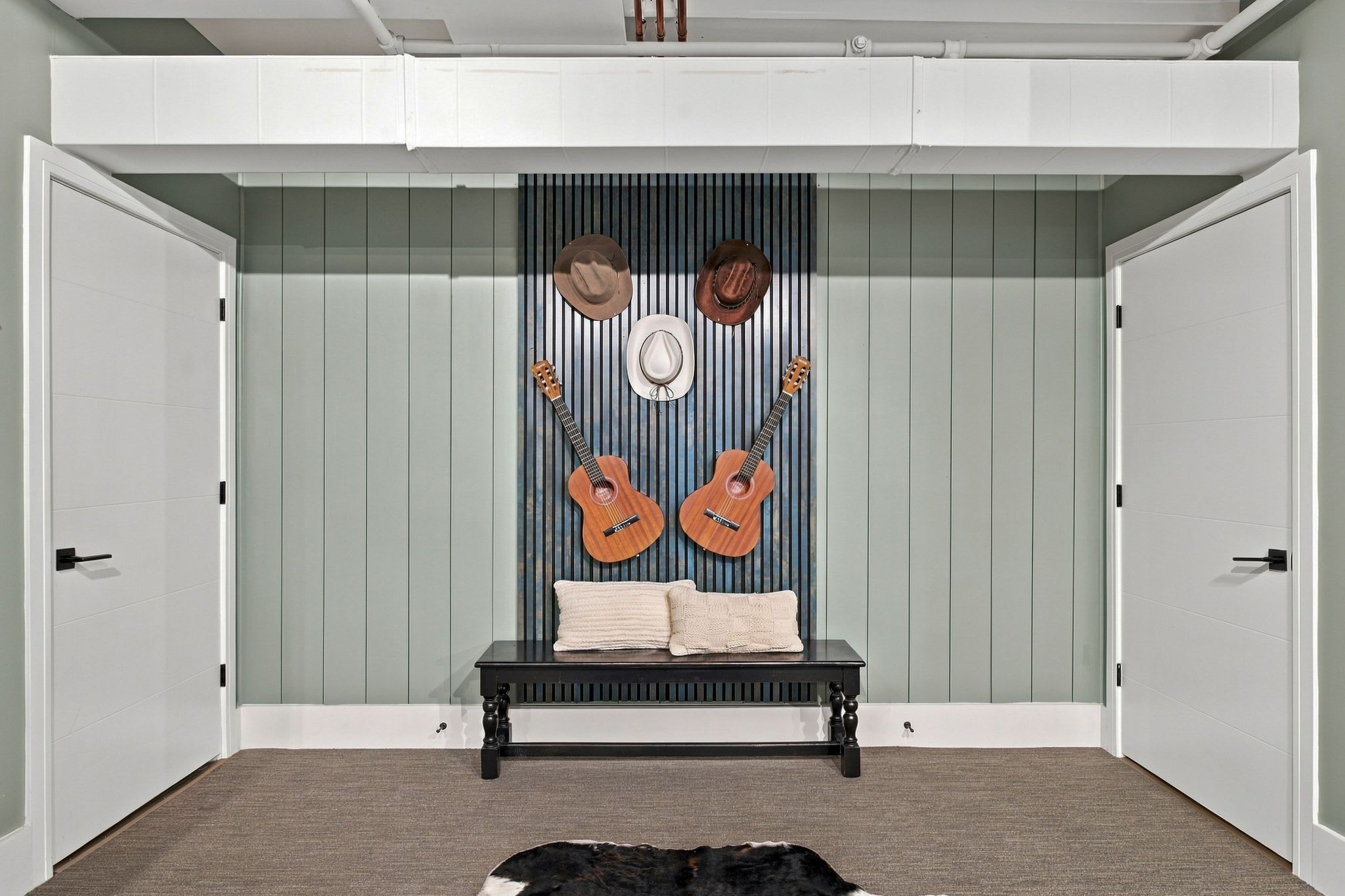 A room with a bench, two guitars, and three hats on a wall.