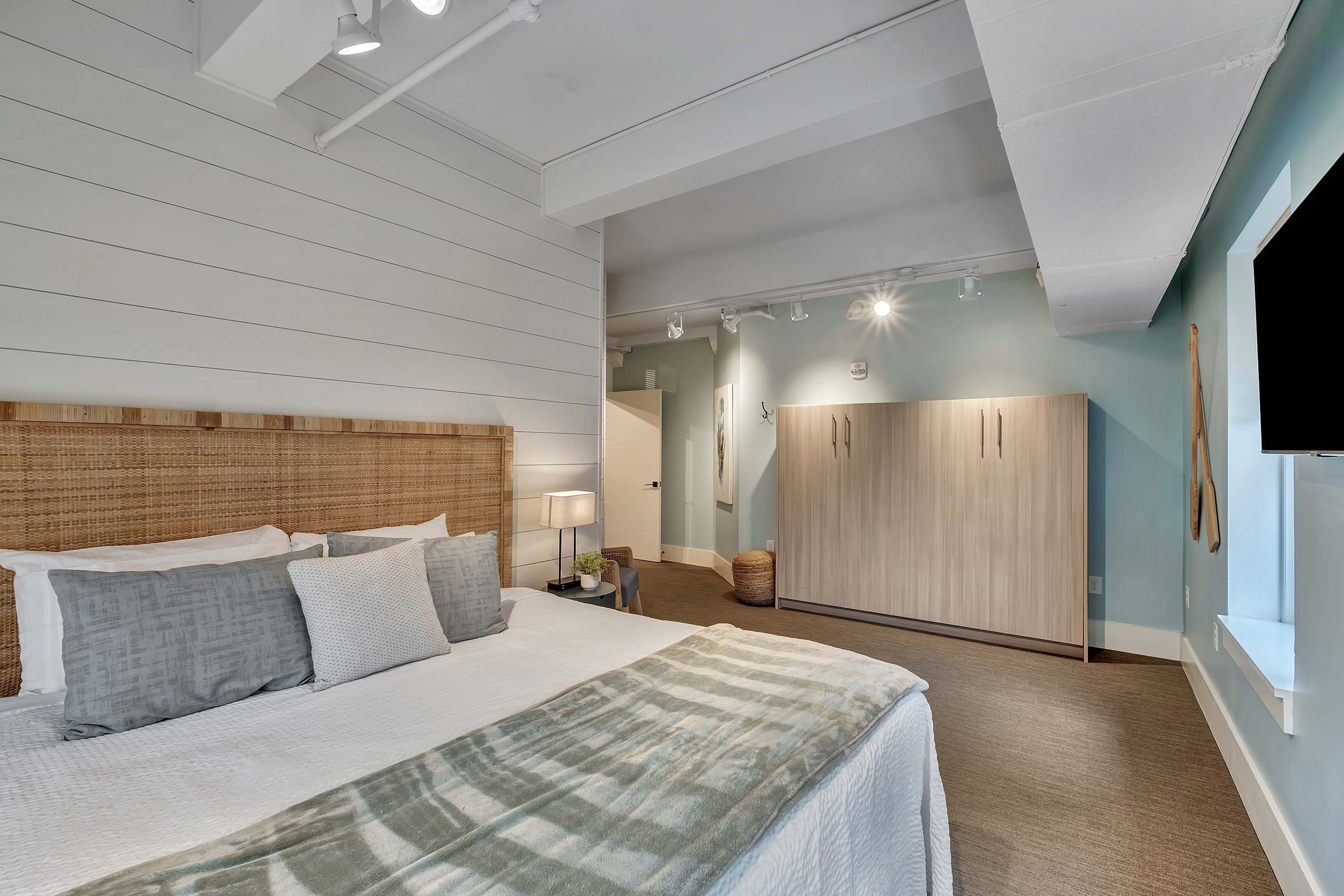 A bedroom with a large bed, a wooden headboard, a wardrobe, and a nightstand with a lamp.