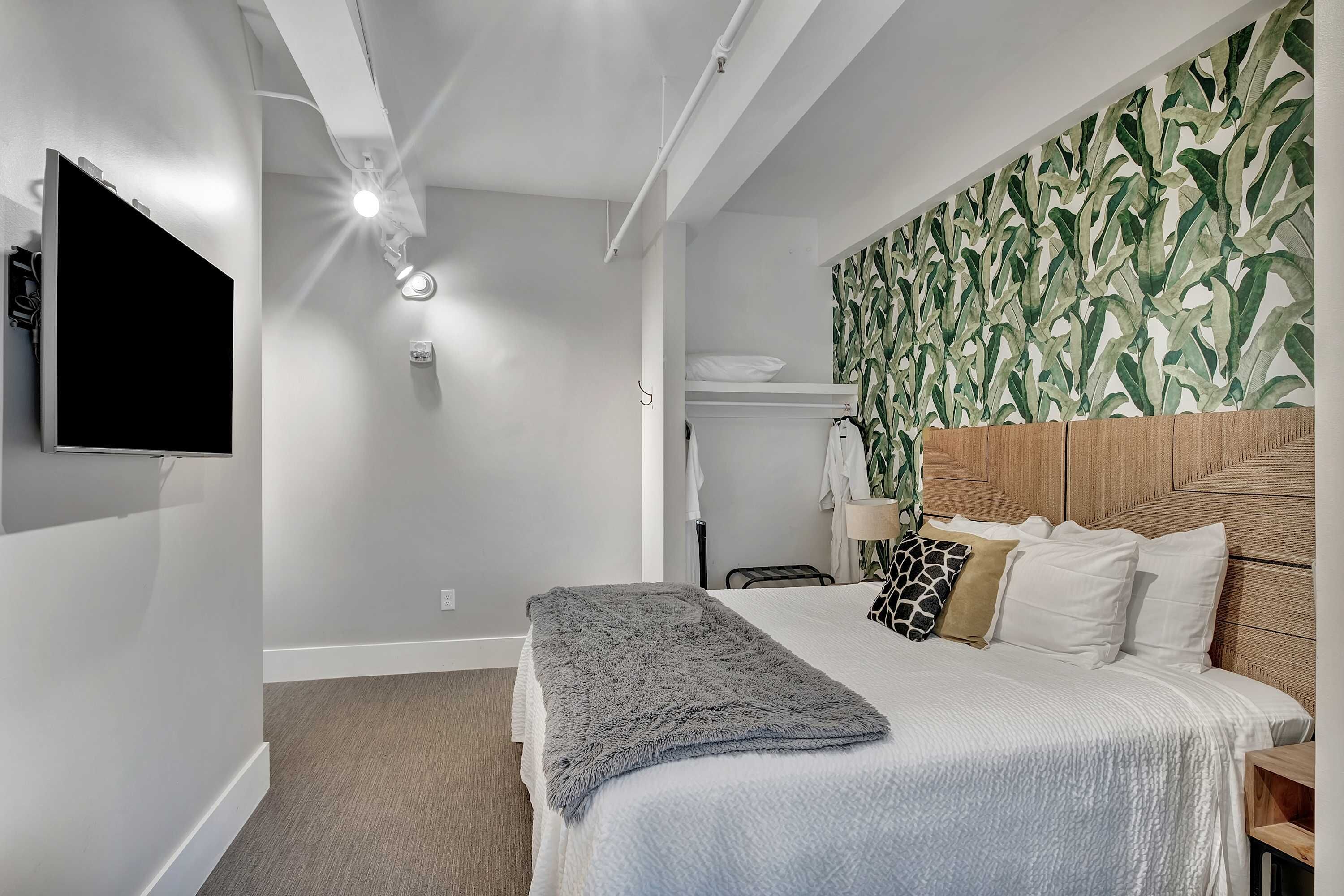 Une chambre à coucher comprenant un lit, un téléviseur, un luminaire au plafond, une étagère fixée au mur et un papier peint à motifs.