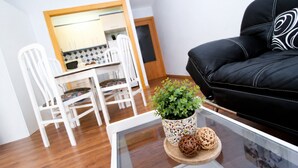 Ein modernes Wohnzimmer mit einem Glastisch, einem schwarzen Ledersofa, weißen Stühlen und einem Essbereich mit einem weißen Tisch und Stühlen.