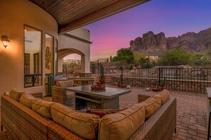 A patio with wicker furniture, a stone wall, and a view of a rocky landscape at sunset.