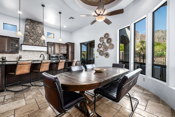 A spacious kitchen with a large dining table, stone accent wall, and large windows offering a view of the outdoors.