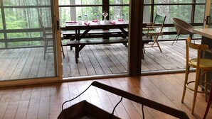 A wooden deck with picnic tables and chairs, large windows with a forest view, and a hanging light fixture. - Forest Hideaway (Keene)