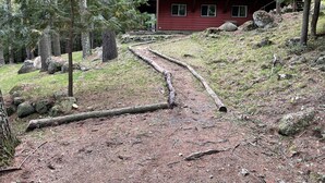 A red cabin with a dirt path leading up to it, surrounded by trees and rocks. - Forest Hideaway (Keene)