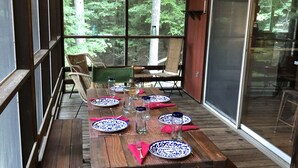 A wooden deck with a dining table set for four, surrounded by chairs, overlooking a forested area. - Forest Hideaway (Keene)