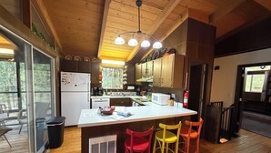 A kitchen with wooden cabinets, a central island, a microwave, and a refrigerator. - Forest Hideaway (Keene)