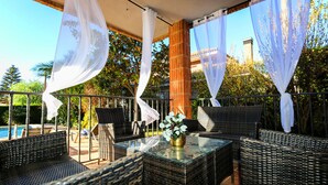 Eine Terrassengruppe im Freien mit Korbmöbeln, einem Glastisch und weißen Vorhängen.