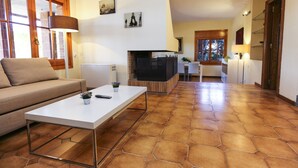 Ein Wohnzimmer mit Sofa, Couchtisch und Kamin. Zwei Lampen, ein Fernseher und ein kleiner Tisch mit einer Pflanze sind ebenfalls vorhanden.