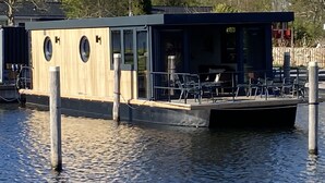 A stationary houseboat with a covered deck and seating area.