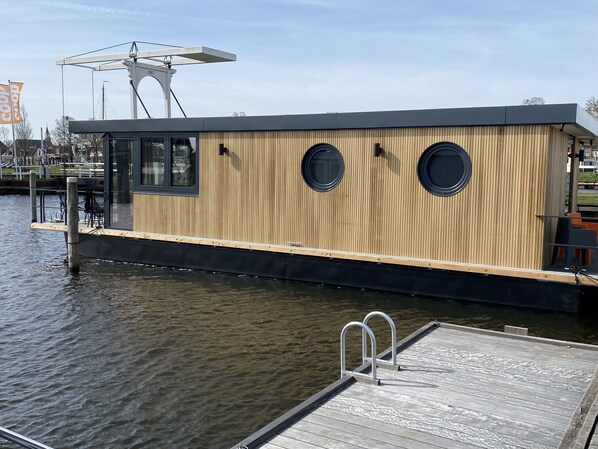 A modern houseboat with a wooden exterior, large windows, and a dock.